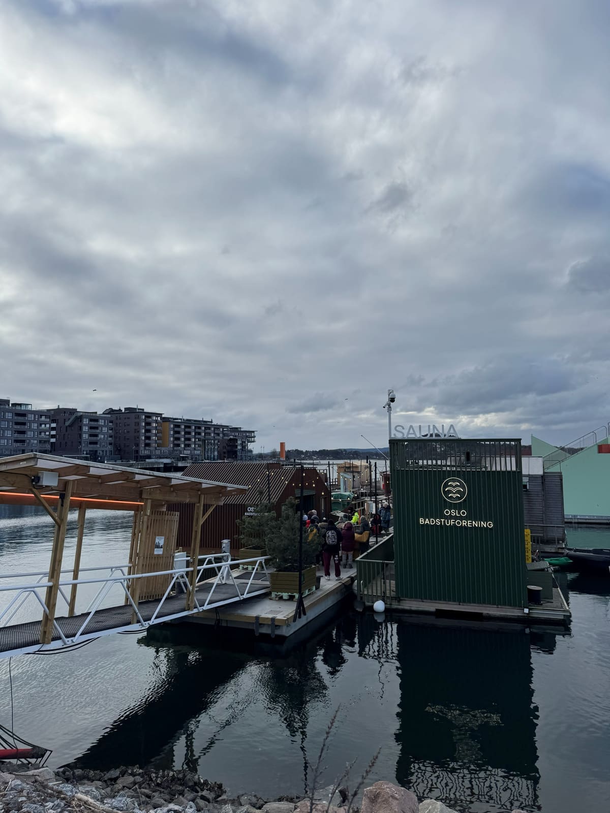 Floating timber saunas moored in Oslo's Bjørvika harbour, apartment blocks along the water behind